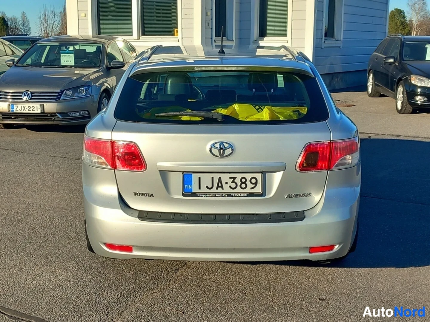 Takaa: Auton takaosa suoraan takaa, rekisterikilpi, hopeinen Toyota Avensis.