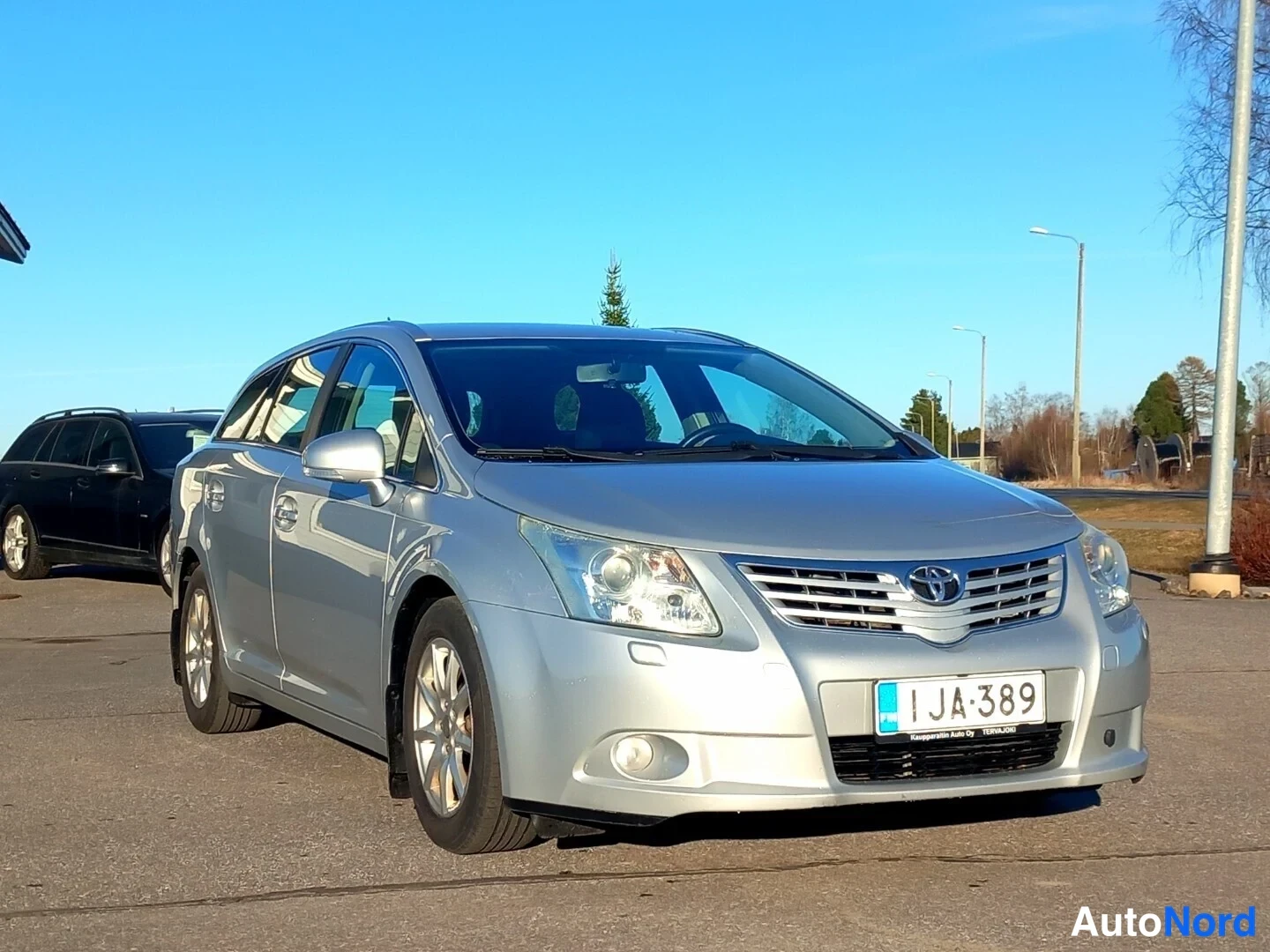Etuviisto, nokka vasemmalle: Toyota Avensis -farmari edestä vasemmasta nurkasta kuvattuna, hopeinen, rekisteritunnus.
