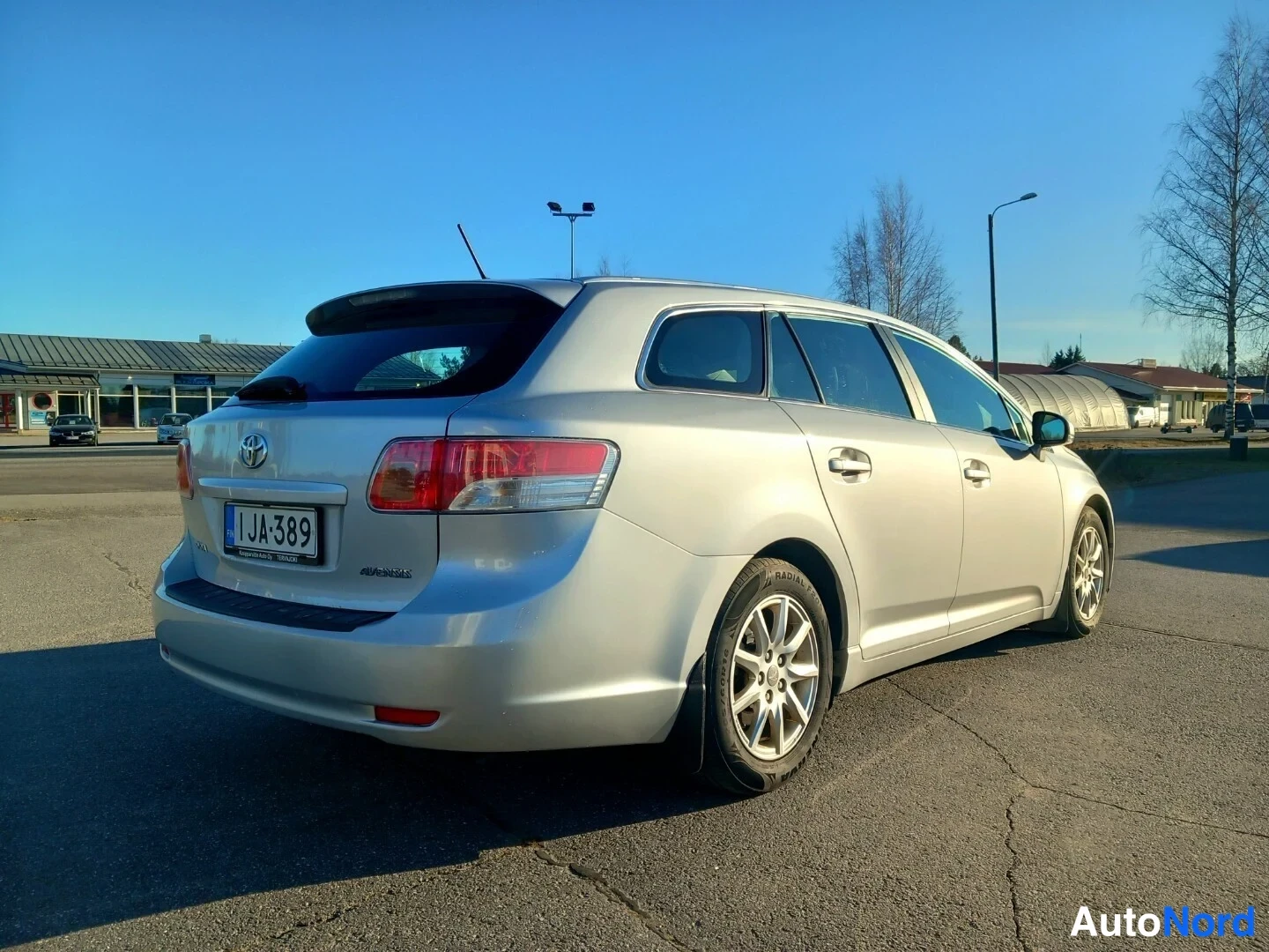 Takaviisto: Hopeanharmaa farmariauto kuvattu takaa viistosti oikealta; rekisterikilpi JA-389 ja Toyota-merkki näkyvät.
