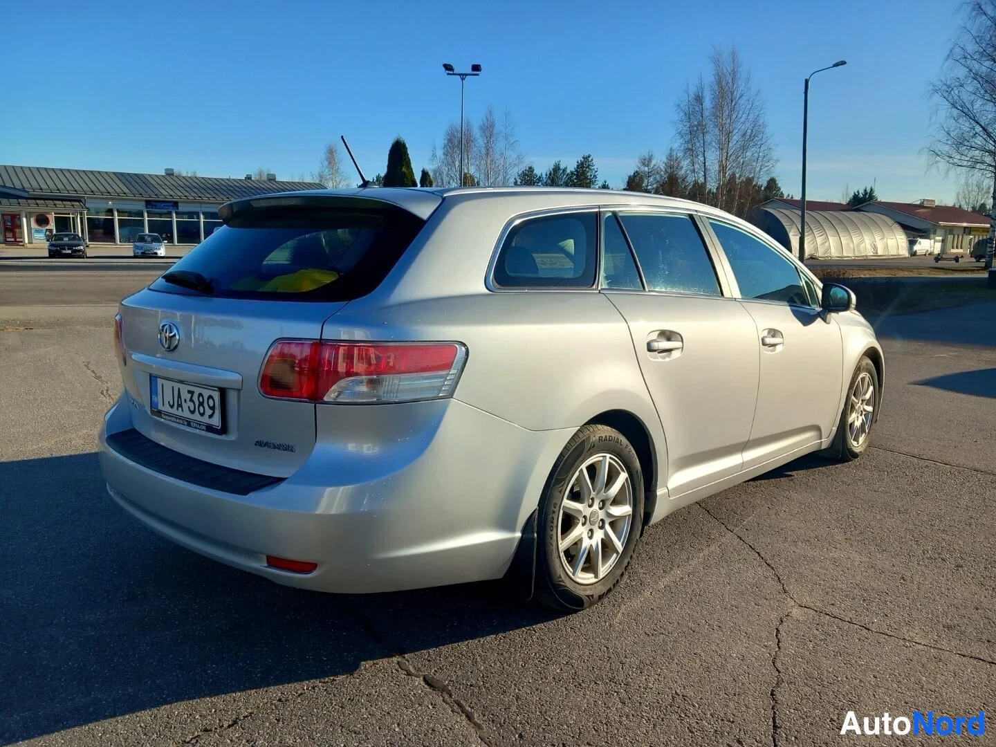 Takaviisto: Hopeanharmaa Toyota-farmariauto takaviistokuvassa oikealta; takavalot ja rekisterikilpi JA-389 näkyvät.
