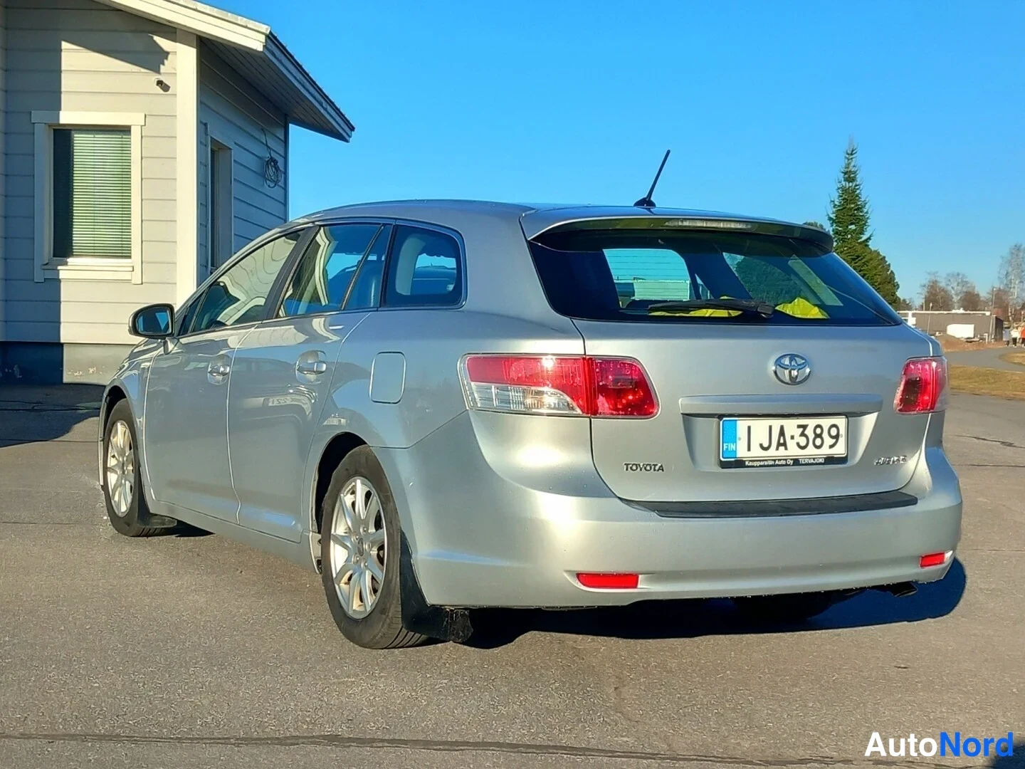 Takaviisto: Hopeanharmaan Toyota-farmariauton takaviistokuva vasemmalta; TOYOTA-teksti ja rekisterikilpi näkyvät takaluukulla.
