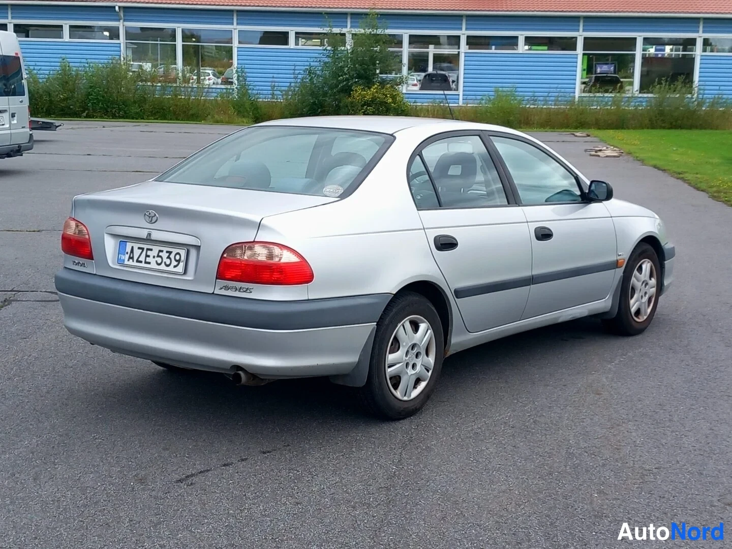 Takaviisto: Hopeahohtoinen sedan takaa viistosti kuvattuna; takavalot, -kilpi ja Avensis-merkintä näkyvät.