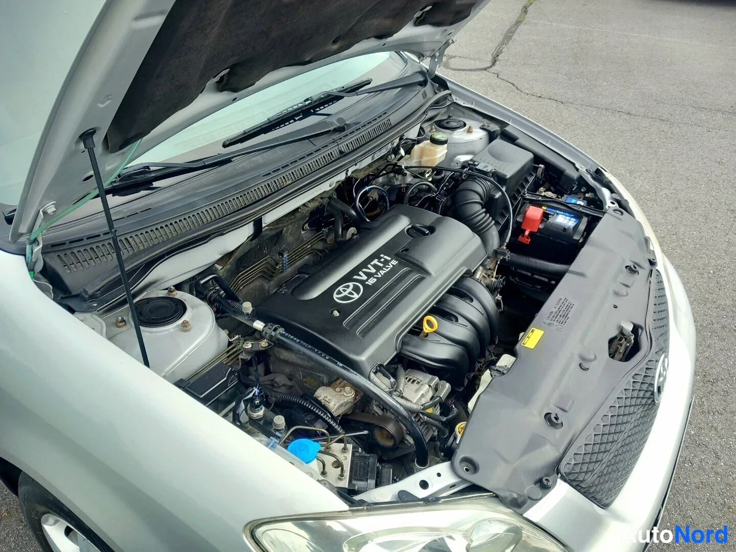 Edestä: Auton avattu moottoritila, kannessa VVT-i 16 VALVE -merkintä, akku ja nestesäiliöt näkyvissä.