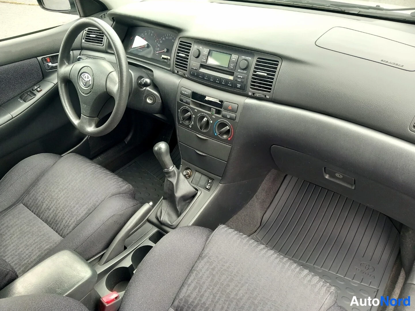 Etuistuimet: Sisäkuva: Toyota-ohjaamo, manuaalivaihteisto, radio ja tummat kangasistuimet.