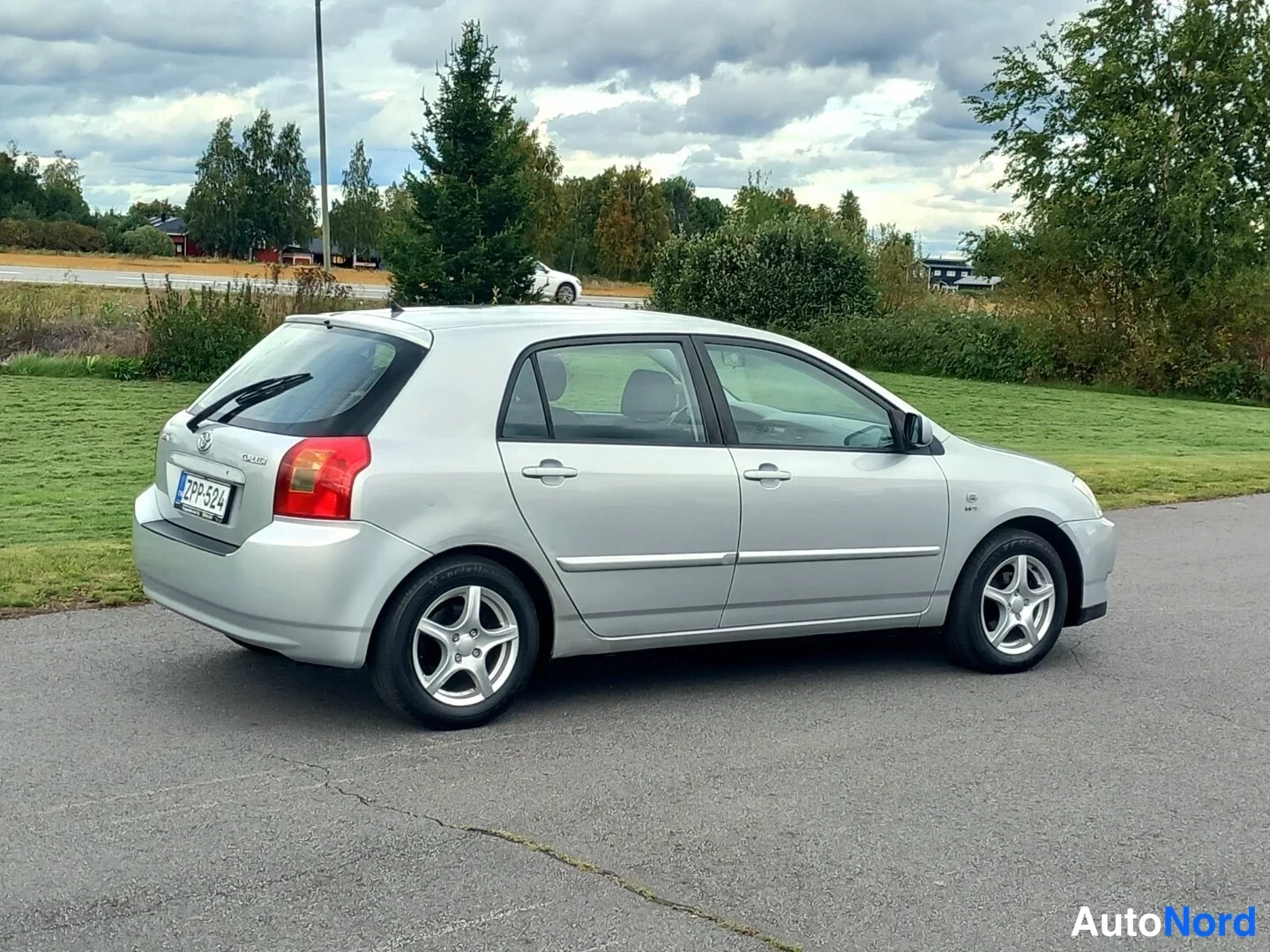 Takaviisto: Hopeanvärinen Toyota Corolla viistosti takaa vasemmalta, rekisteritunnus, pysäköitynyt asfaltille.