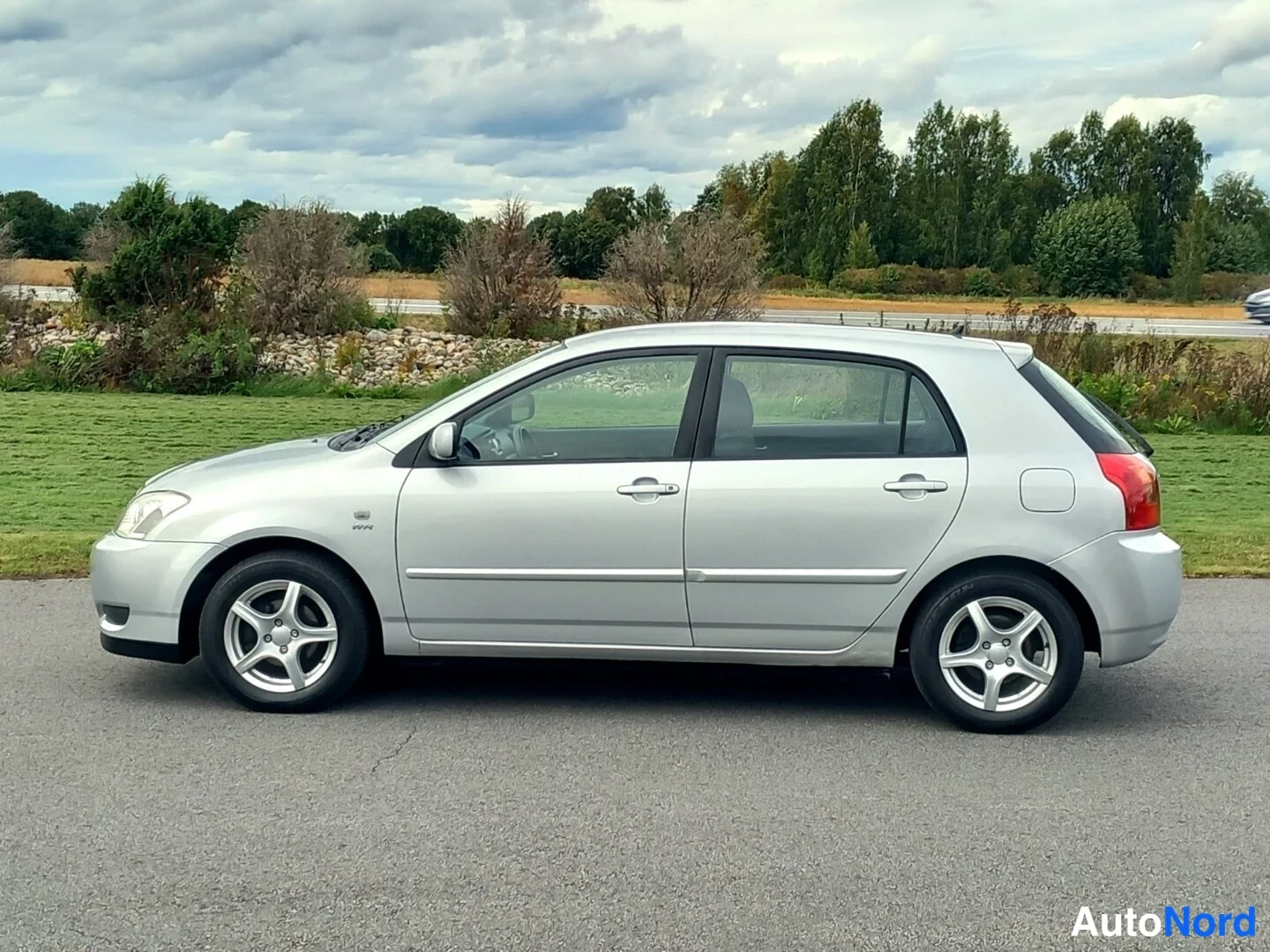 Sivulta: Hopeanvärinen Toyota Corolla -viistoperä sivusta sivuotoksessa parkkipaikalla, kokonainen auto näkyvissä.