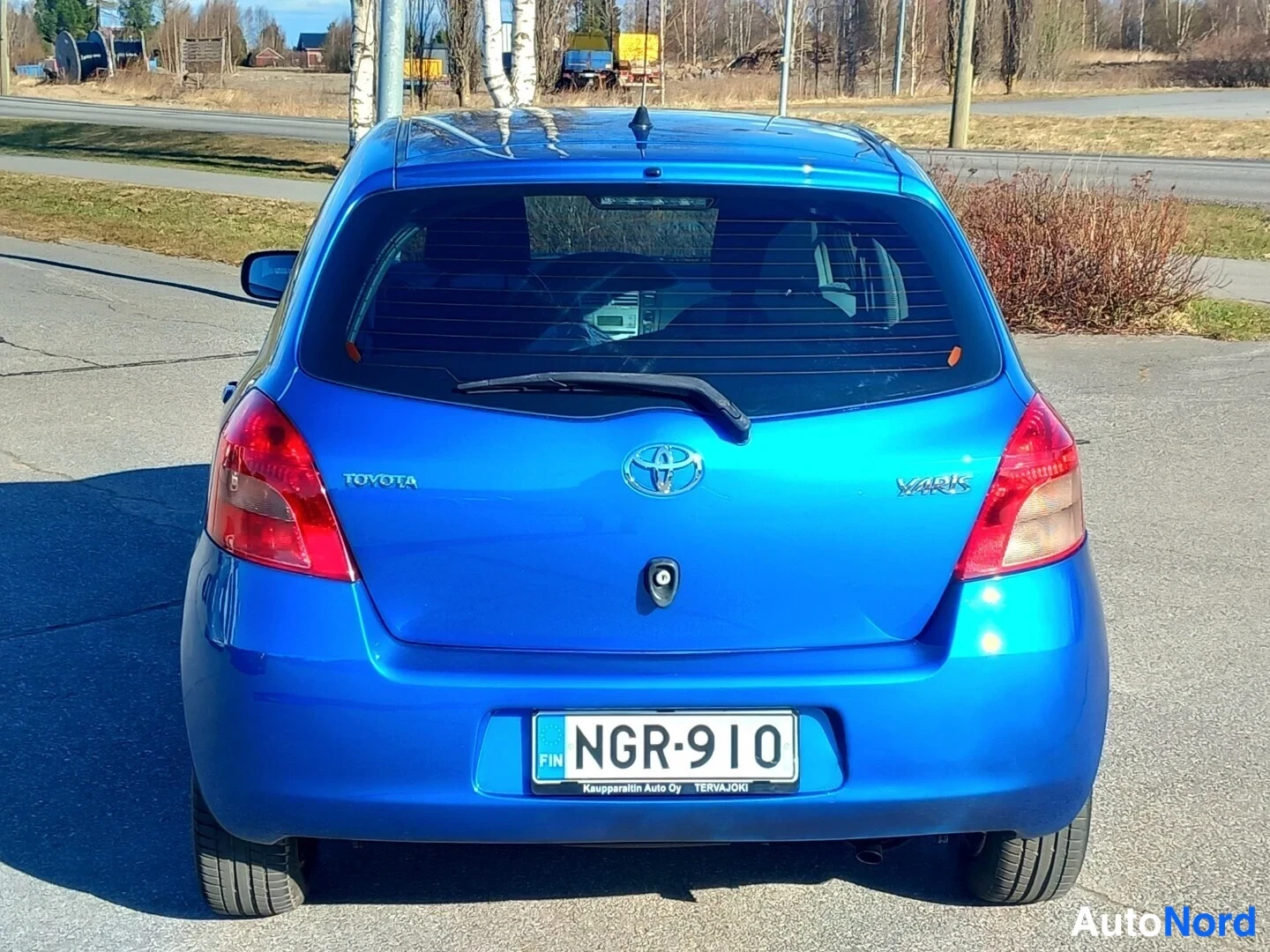 Takaa: Sininen Toyota Yaris suoraan takaa kuvattuna: takaluukussa Toyota- ja Yaris-merkit, punaiset takavalot, takatuhruholkki ja rekisterikilpi.