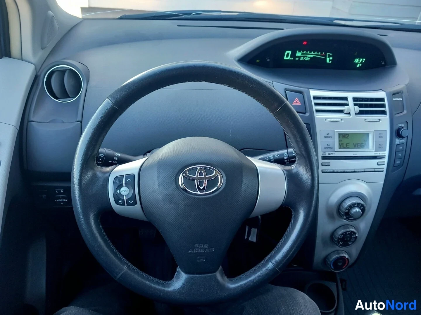 Etuistuimet: Ohjaamokuvassa näkyy Toyota-pyörän takaosassa olevat monitoimiohjausnappulapainikkeet ja keskikonsolissa oleva radiolaite sekä ilmastointilaitteiston kytkimet.