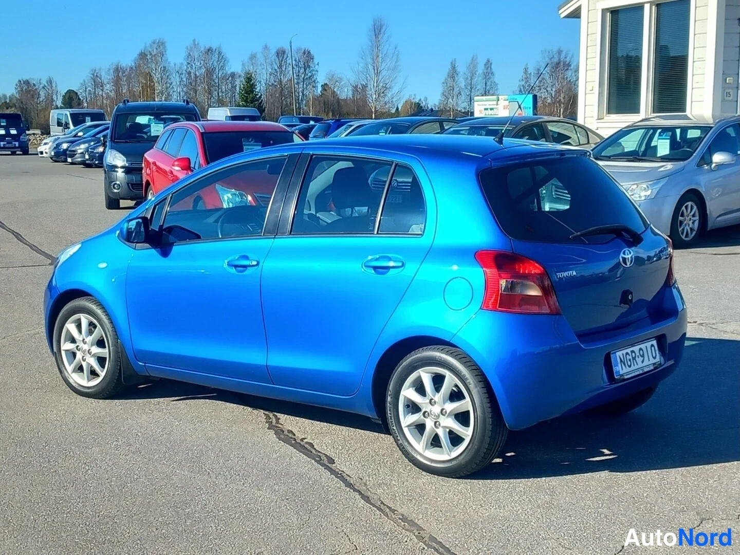 Takaviisto: Sininen Toyota Yaris -henkilöauto kuvattu takaa oikealta kulmasta, rekisterikilpi ja takaluukun Toyota-logo näkyvät.