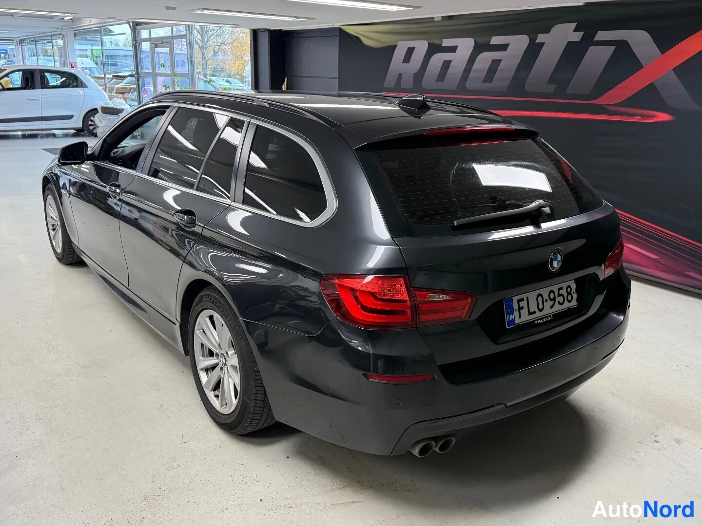 Takaviisto: Tummanharmaa BMW 5 -farmari takakulma vasemmalta, takavaloissa ja rekisterikilpi FL0-958.