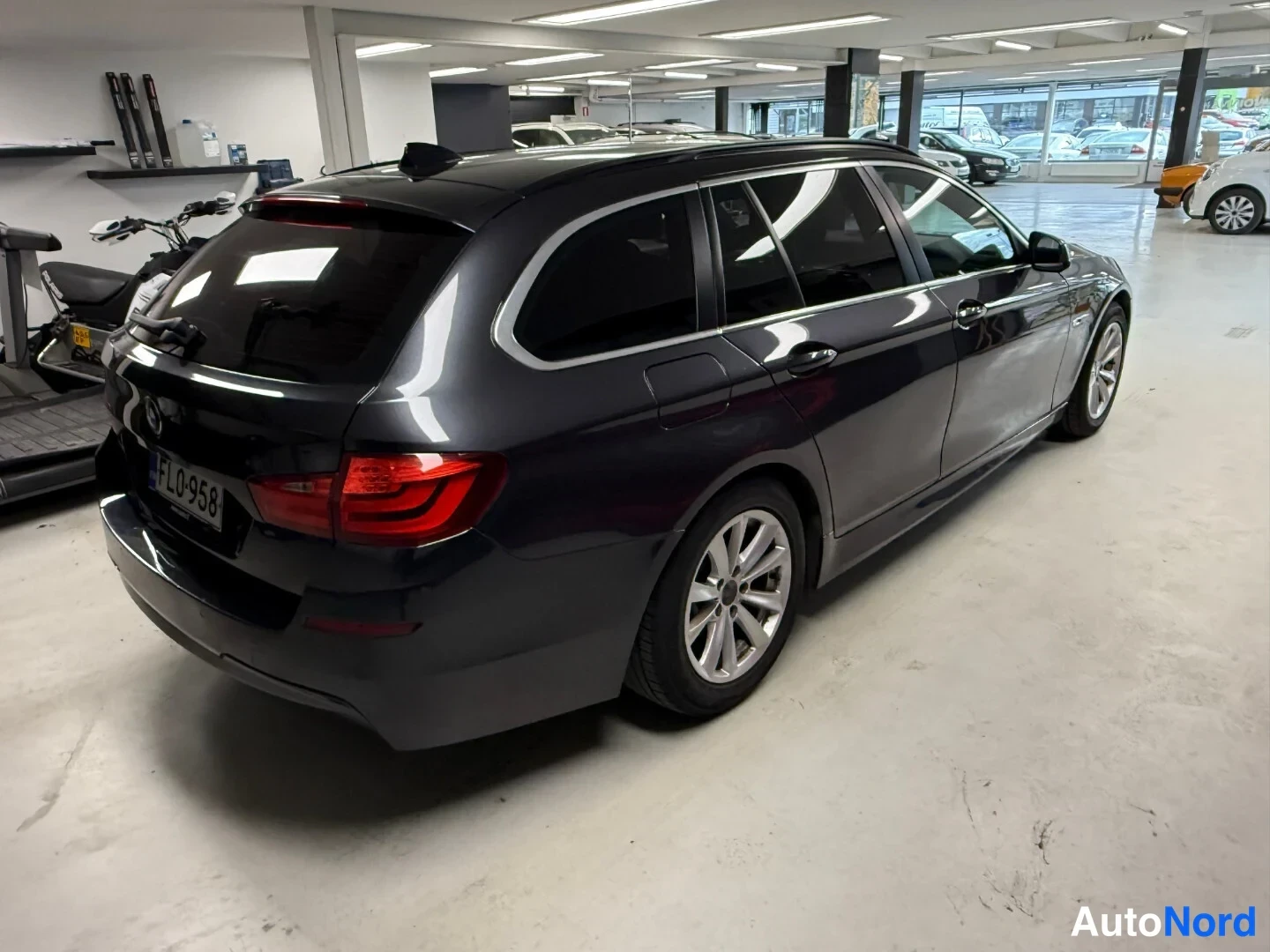 Takaviisto: Tummanharmaa BMW 5 -farmari takakulmalta autotallissa, rekisterikilpi FL0-958.