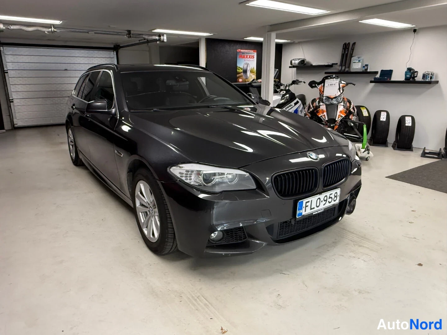 Etuviisto, nokka oikealle: Tummanharmaa BMW 5 -farmari kolmannelta etukulmalta autotallissa, rekisterikilpi FL0-958.