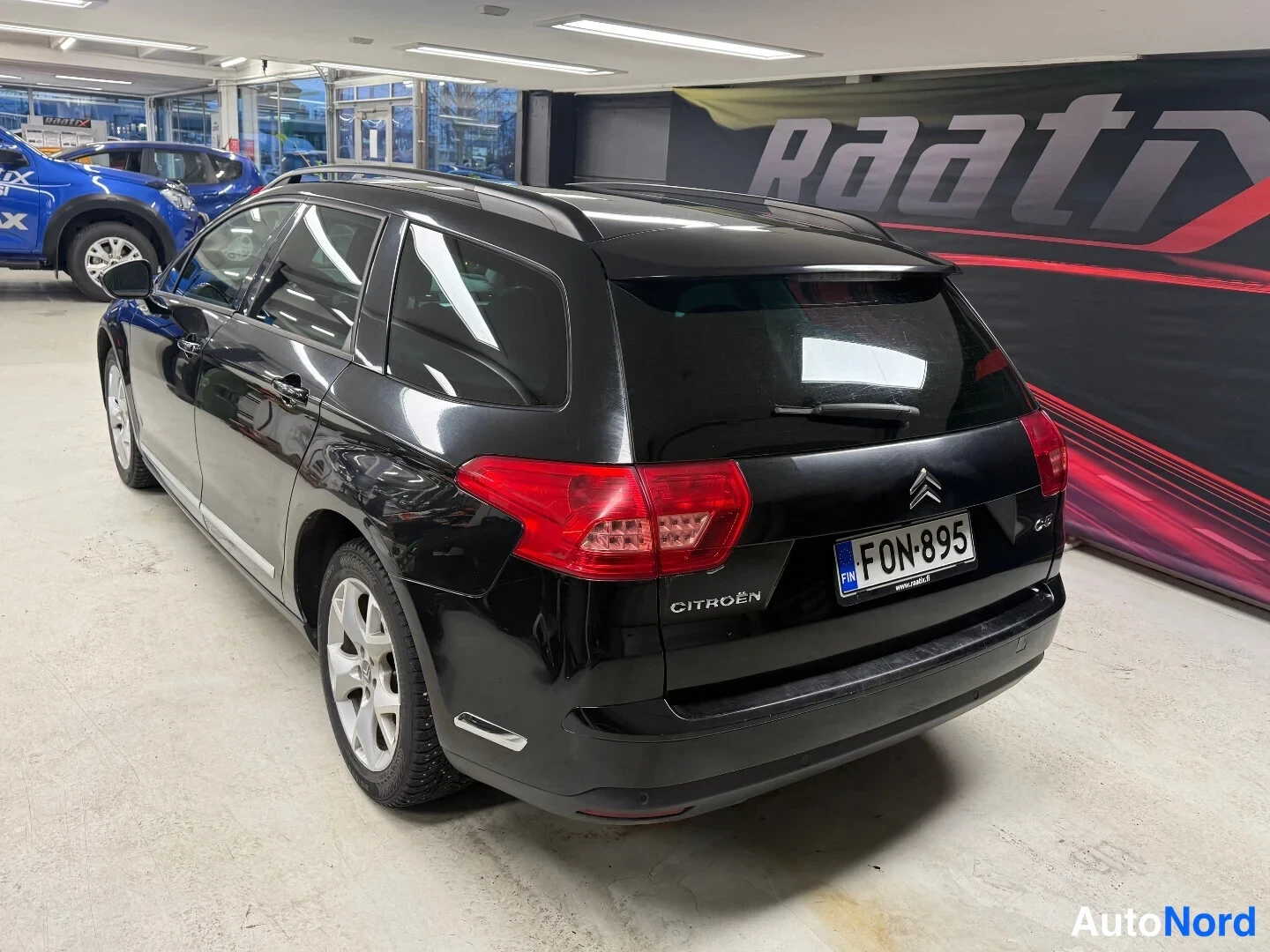 Takaviisto: Mustan farmariauton takakulma sisätiloissa, Citroën-merkki ja rekisterikilpi.