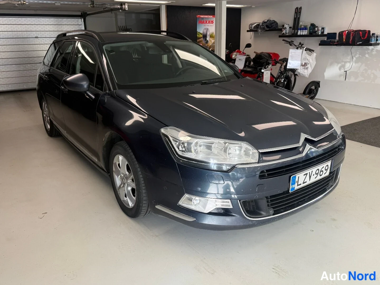Etuviisto, nokka oikealle: Citroen C5 -farmari edessä oikealta kolmivartaloasennossa autotallissa, rekisterikilpi ja hopeavanteet näkyvät.