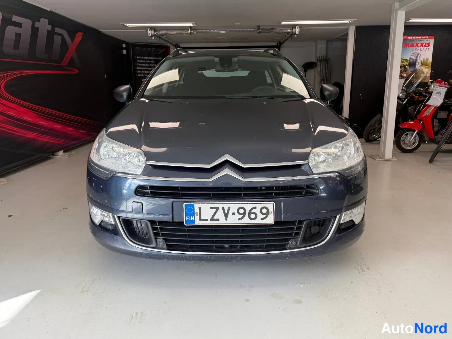 Edestä: Citroën C5 -farmariauto edestäpäin kuvattuna sisätiloissa, rekisterikilpi.