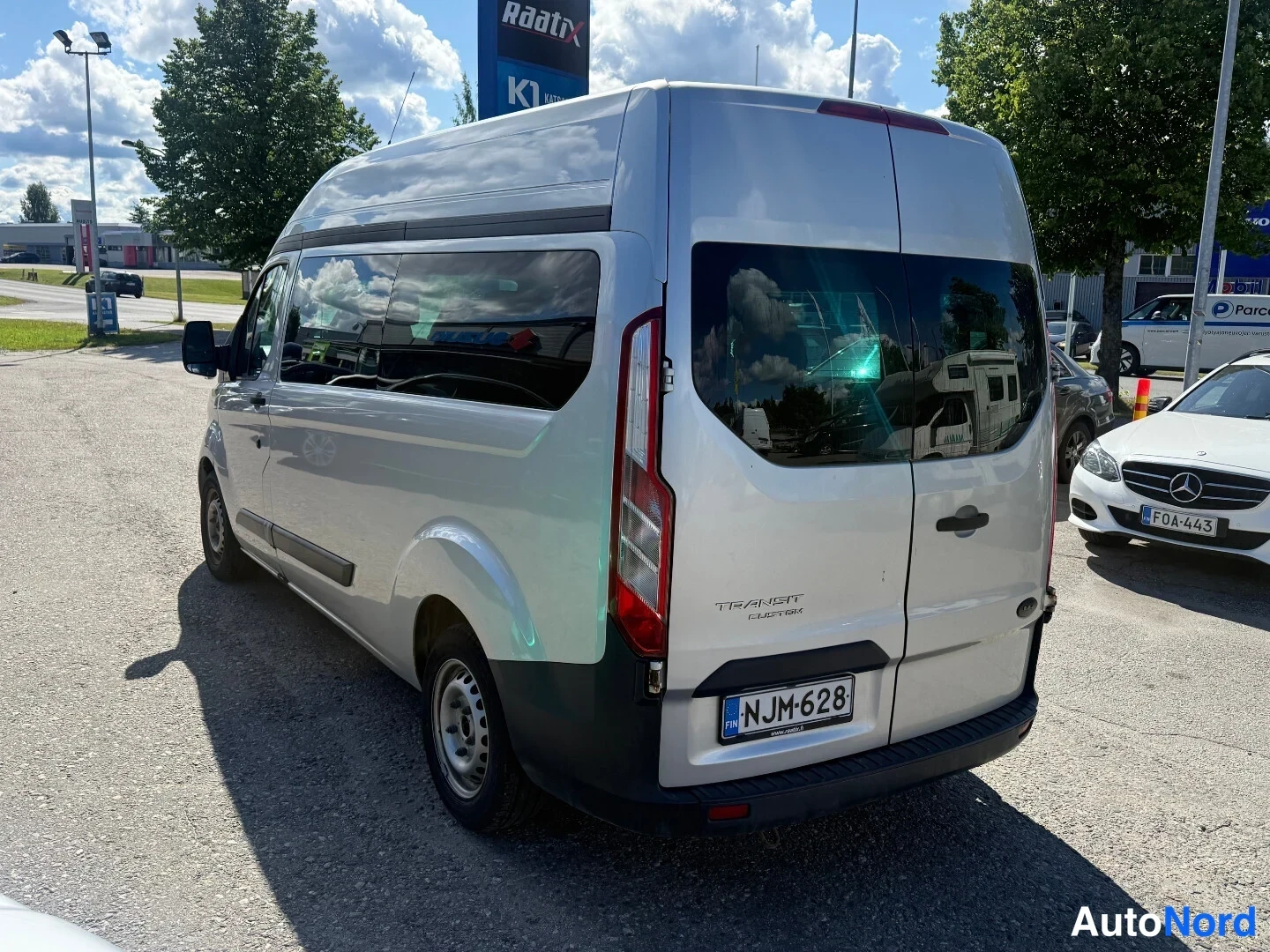 Takaviisto: Hopeanvärinen Ford Transit Custom -pakettiauto takaviistöstä, rekisterikilpi ja Transit Custom -teksti takaluukussa.