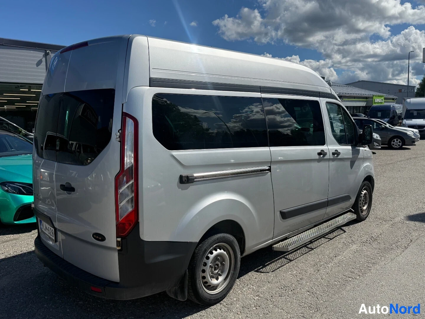 Takaviisto: Hopeanvärinen Ford Transit Custom -pakettiauto takaviistöstä oikealta, tummennetut sivuikkunat ja ritiläinen sivulauta.