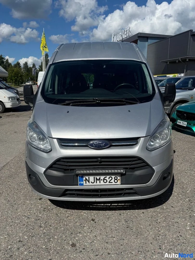 Edestä: Ford Transit Custom -pakettiauton etupää suoraan edestä kuvattuna; hopea kori, Ford-merkki säleikössä ja suomalainen rekisterikilpi.
