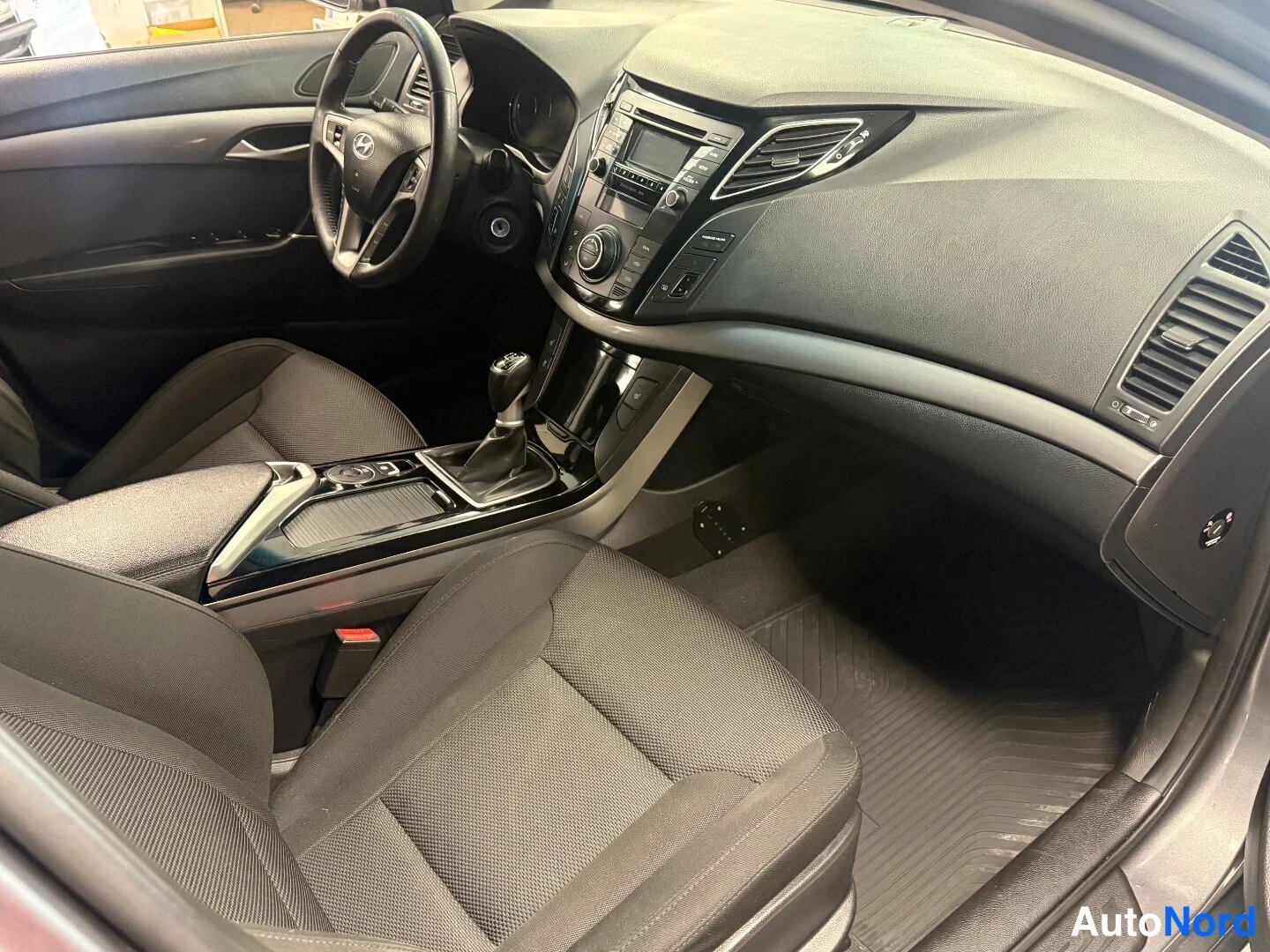 Muu: Ajetun Hyundai i40:n matkustamon etuosa: tumma kojelauta,Hyundai-merkkinen ohjauspyörä, automaattivaihteen valitsin ja kaksi tummaa kangastuolia.