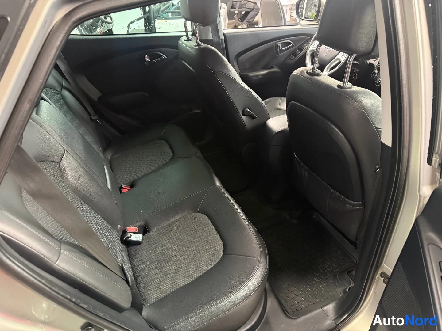 Muu: Hyundai ix35:n takaistuin kuvattuna takaa vasemmalta avatusta ovesta: tumma penkki, turvavyöt ja musta lattiamatto.