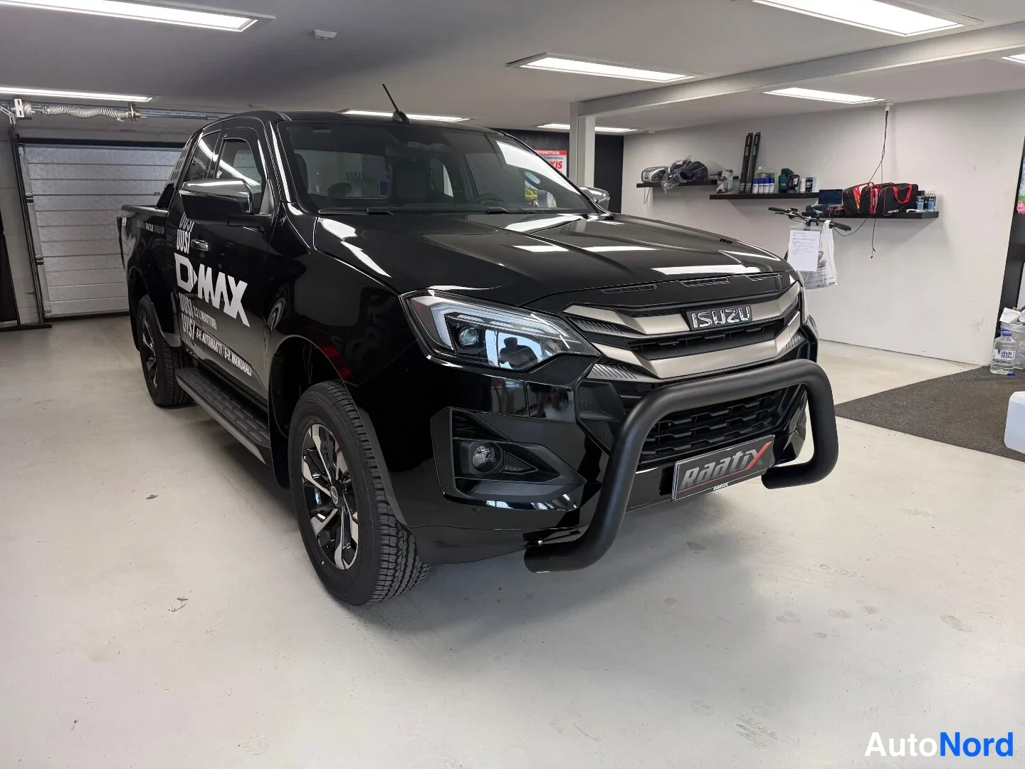 Etuviisto, nokka oikealle: Musta Isuzu D-Max -ava-aurinkoa edestä oikealta kuvattuna, keulakaari asennettuna.