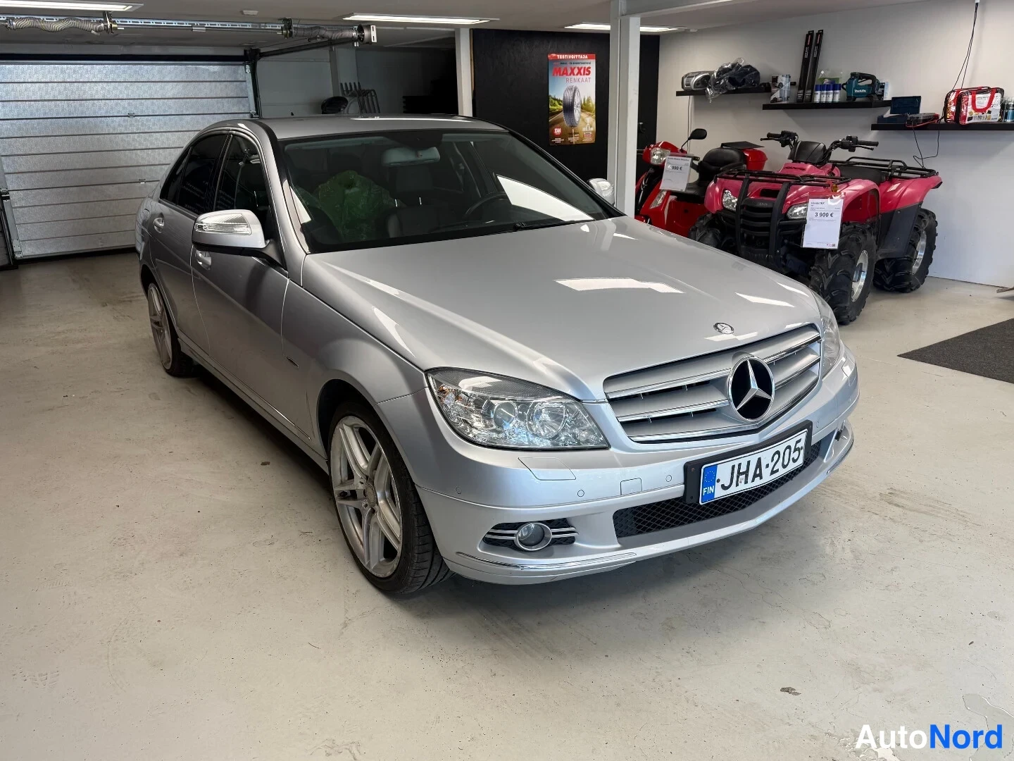 Etuviisto, nokka oikealle: Hopeanvärinen Mercedes-Benz C-sedan etualalla autotallissa, keula oikealle näkyvissä rekisteritunnus.