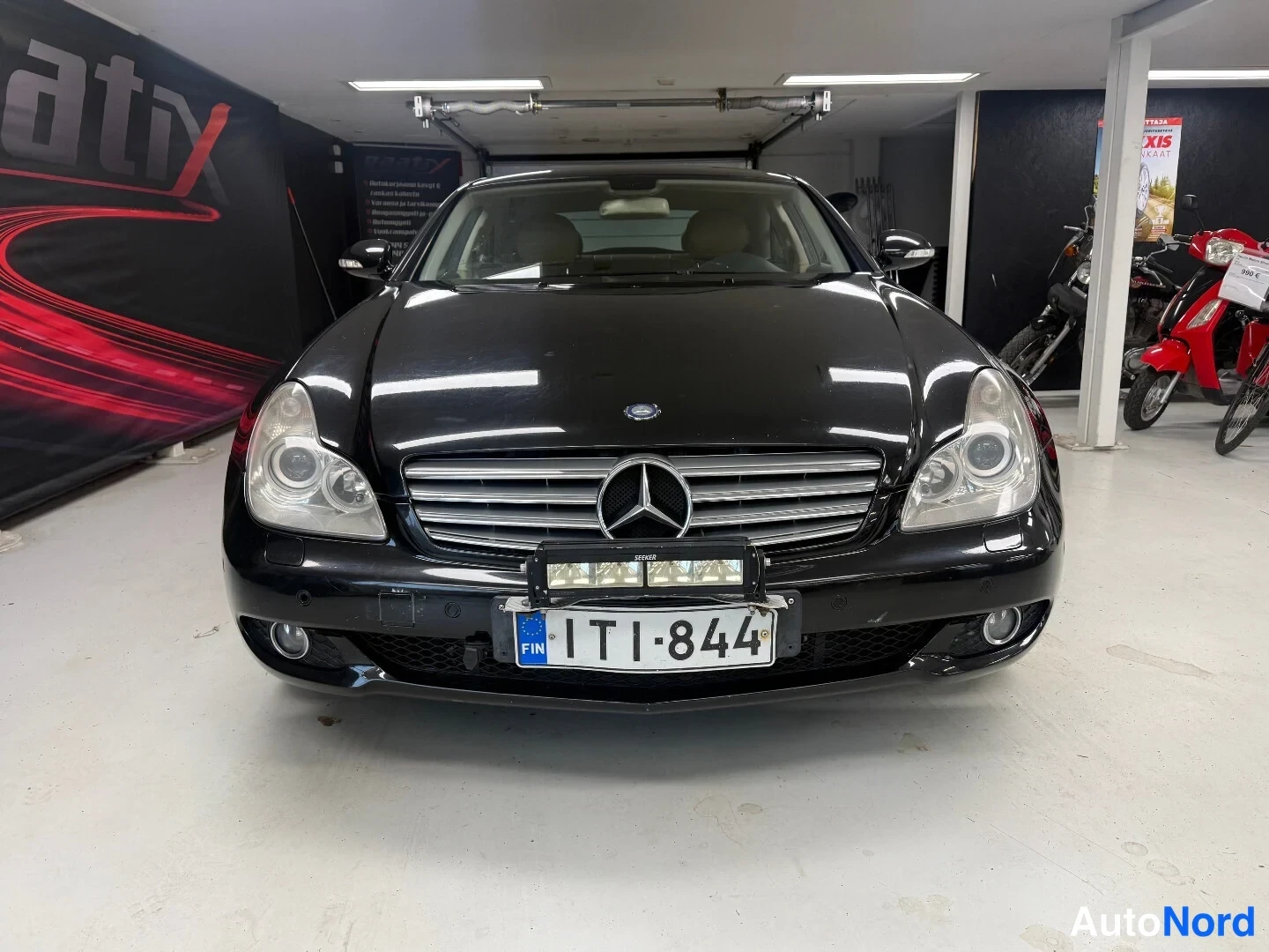 Edestä: Mustan Mercedes-Benzin etupää kuvattuna suoraan edestä; konepellin alla olevassa kojeessa kiinteä lisävalo ja edessä FIN-tunnusmerkillä varustettu rekisterikilp