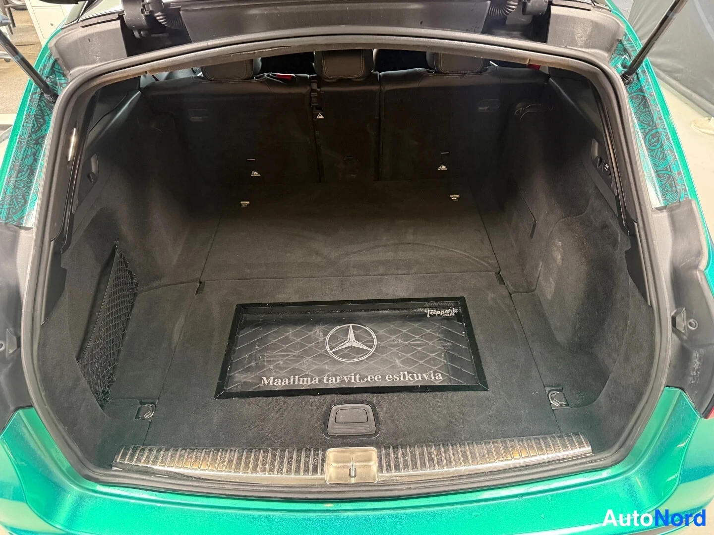 Takaa: Auki oleva tavaratila, tumma matto ja Mercedes-tunnus, auto vihreä