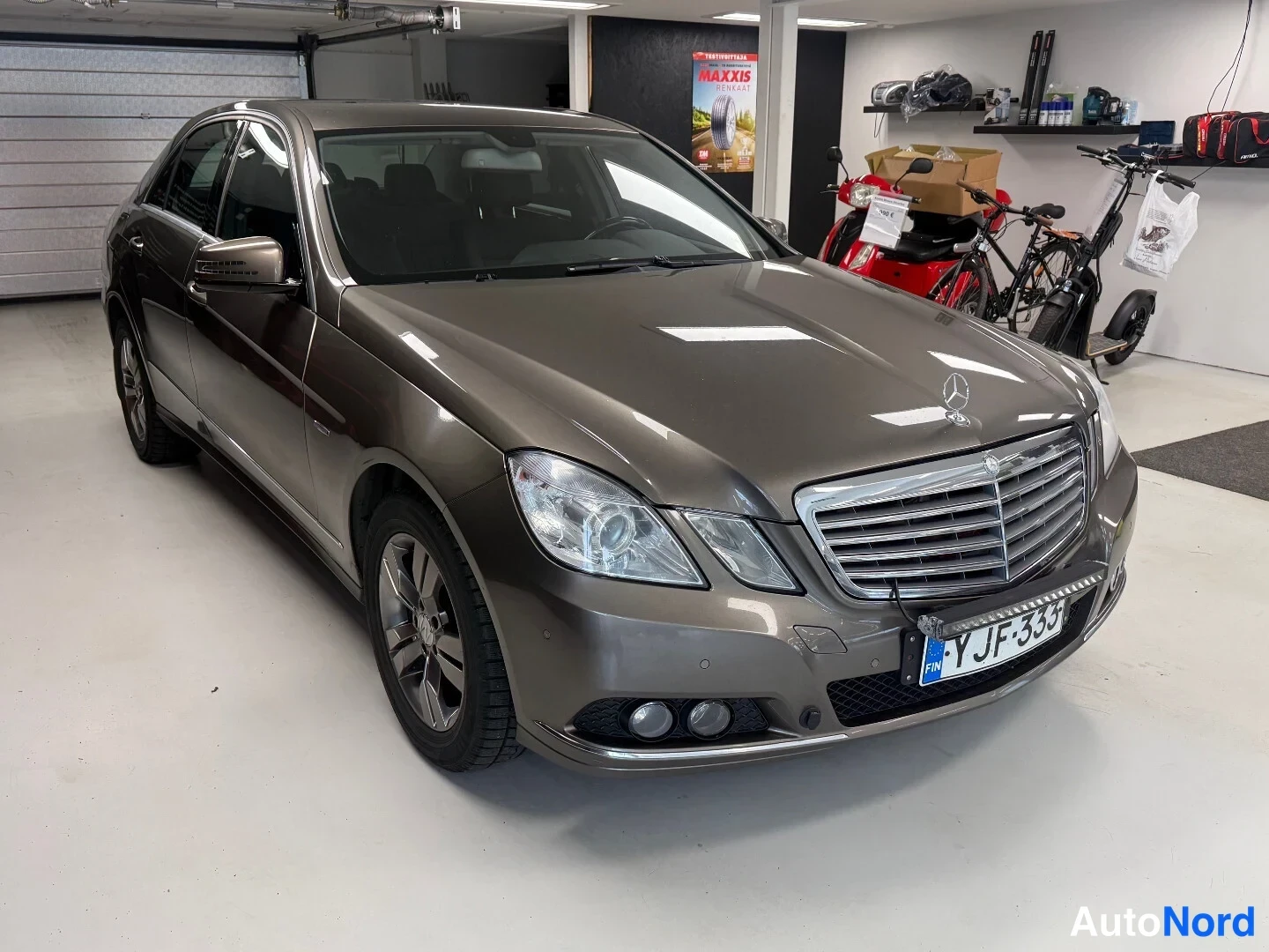 Etuviisto, nokka oikealle: Mercedes-Benz E-sarjan sedan etuviistosta oikealta, keulagrilli ja ajovalot näkyvissä hallissa.