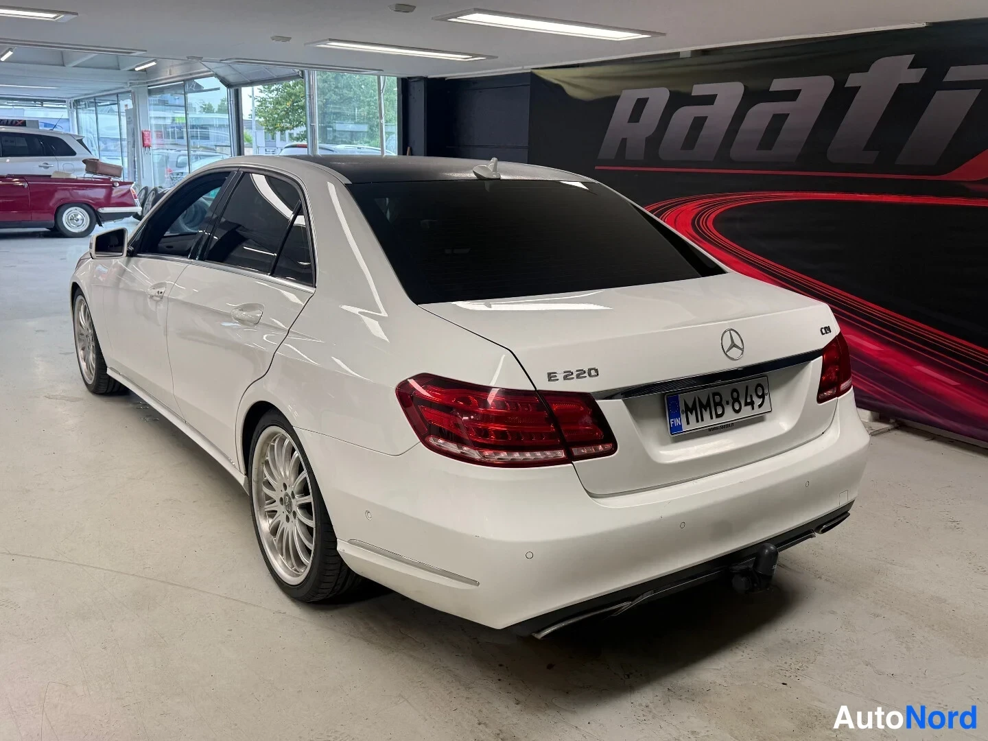Takaviisto: Valkoisen Mercedes-Benz E-sarjan sedanin takakolmasosanäkuva, rekisterikilpi, taki- ja kyljenäkymä sisätiloissa.