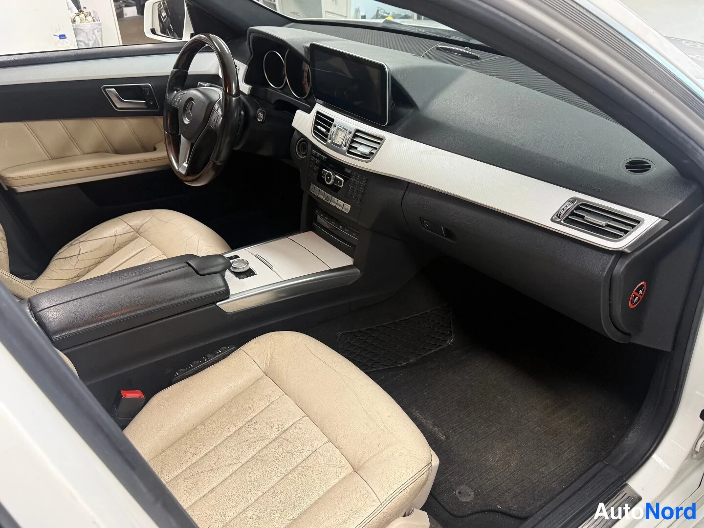 Muu: Uusi kuva Mercedes-Benzin ohjaamosta: beige nahkaistuimet, tumma kojelauta, keskinäyttö ja matkatavaratila lattiamatoilla.