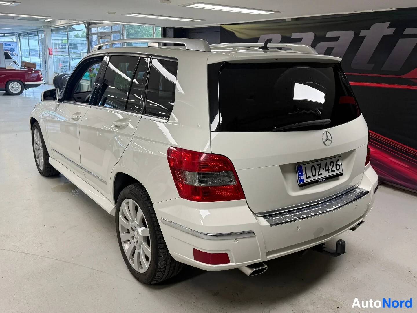 Takaviisto: Valkoisen Mercedes-Benz GLK -maasturin takakolmeneljäsosakuva oikealta sisätiloissa; takana hinauskoukku ja rekisteritunnus.