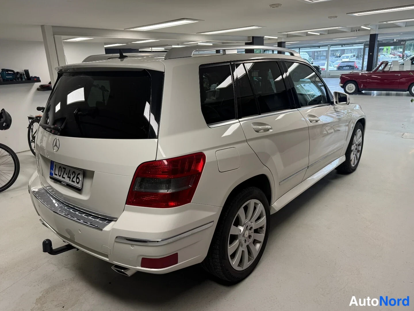 Takaviisto: Valkoisen Mercedes-Benz GLK -maasturin takakolmeneljäsosakuva vasemmalta sisätiloissa; takana hinauskoukku ja rekisteritunnus.