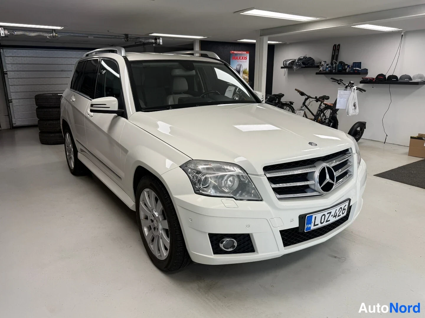 Etuviisto, nokka oikealle: Valkoinen Mercedes-Benz GLK -maasturista kolmeneljäsosakuva edestä oikealta sisätiloissa; rekisteritunnus.