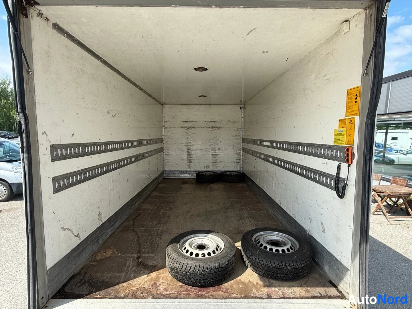 Tavaratila: Cargo area of the white van showing a flat floor with wooden boards near the opening and two spare wheels lying on them. White interior walls feature metal load