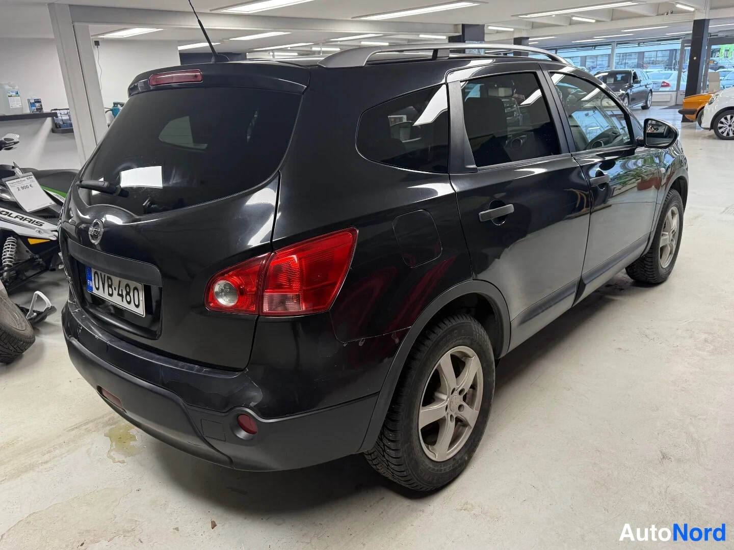 Takaviisto: Mustan Nissan Qashqai+2:n takakulma sisätiloissa, takavalot ja rekisterikilpi näkyvät.