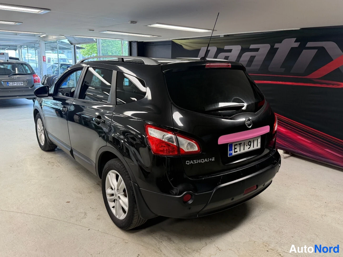 Takaviisto: Nissan Qashqai+2 takakulmasta vasemmalta, musta, rekisteri, takaluukussa QASHQAI+2-teksti.