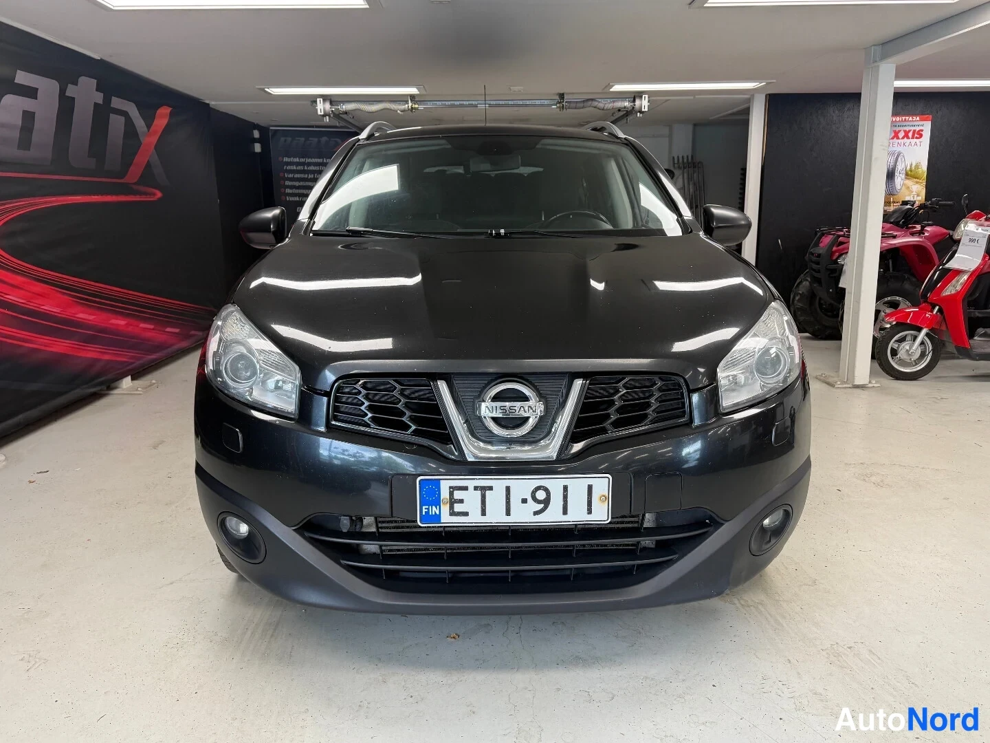 Edestä: Sama etunäkymä Nissan Qashqai +2 -autosta, rekisterikilpi ja Nissan-logo näkyvät selvästi.