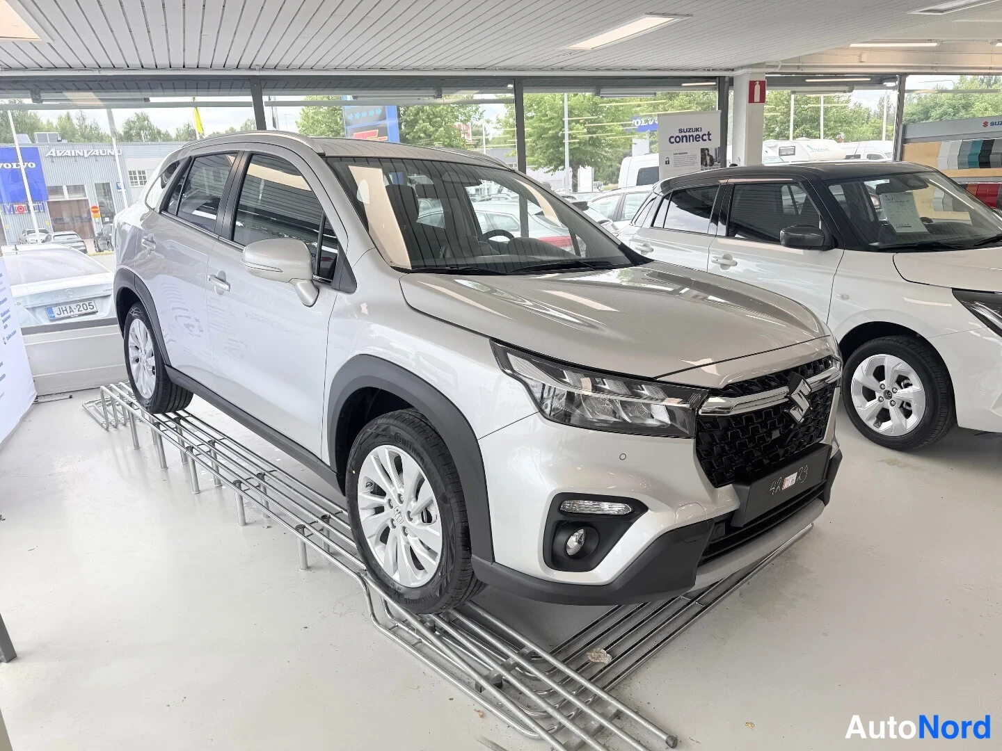 Etuviisto, nokka oikealle: Suzuki S-Cross hopeanvalkoinen etukulmassa myyntitilassa