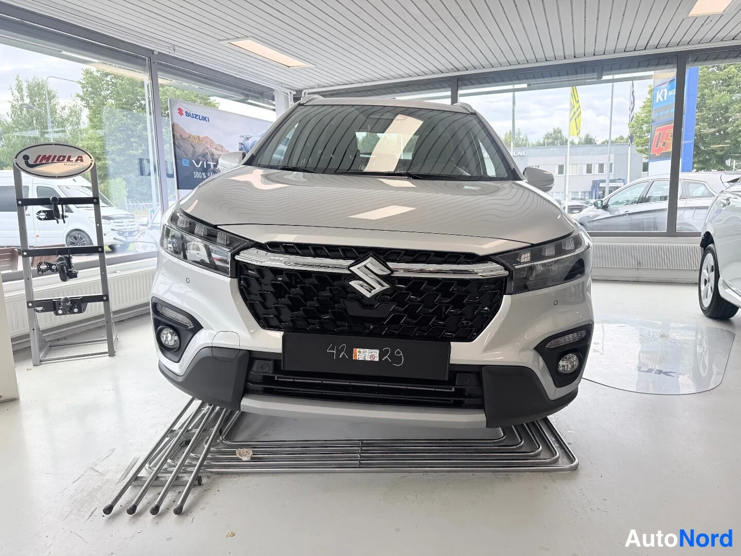 Edestä: Auton etupästä suoraan edestä kuvattu: valkoinen koripelti, musta mendiverkko etugrilli Suzuki-embleemillä, ohuet LED-ajovalot ja sumuvalot puskurin kulmissa.