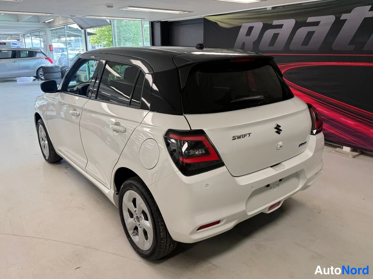 Takaviisto: Valkoinen Suzuki Swift takaa vasemmalta, SWIFT-teksti ja Suzuki-logo takaluukussa.
