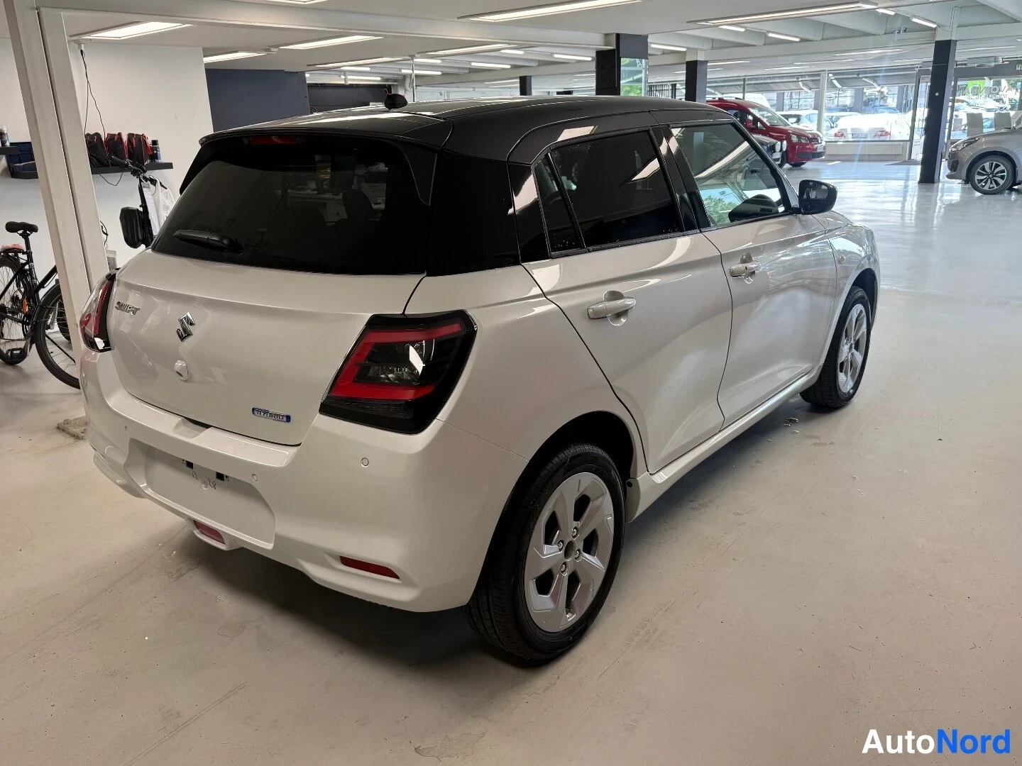 Takaviisto: Valkoinen hatchback takaa ja oikealta sivulta kuvattuna: musta katto, punaiset takavalot ja Suzuki-merkki takaluukussa.