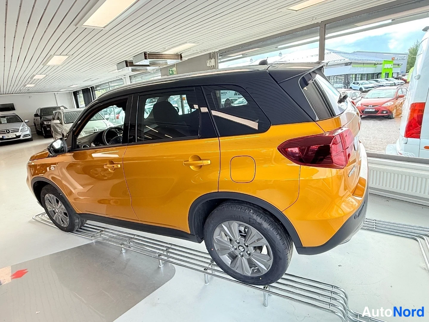 Takaviisto: Oranssin Suzukin takakolmasosa ja oikea kylki; musta katto ja takavalot näkyvät autonäyttelyssä.