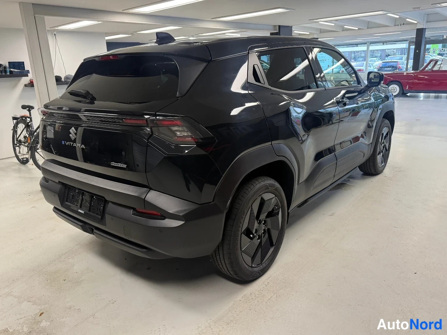 Takaviisto: Musta Suzuki e-Vitara takaa ja vasemmalta sivulta nähtynä autonhallissa, e-VITARA-merkintä takaluukussa.