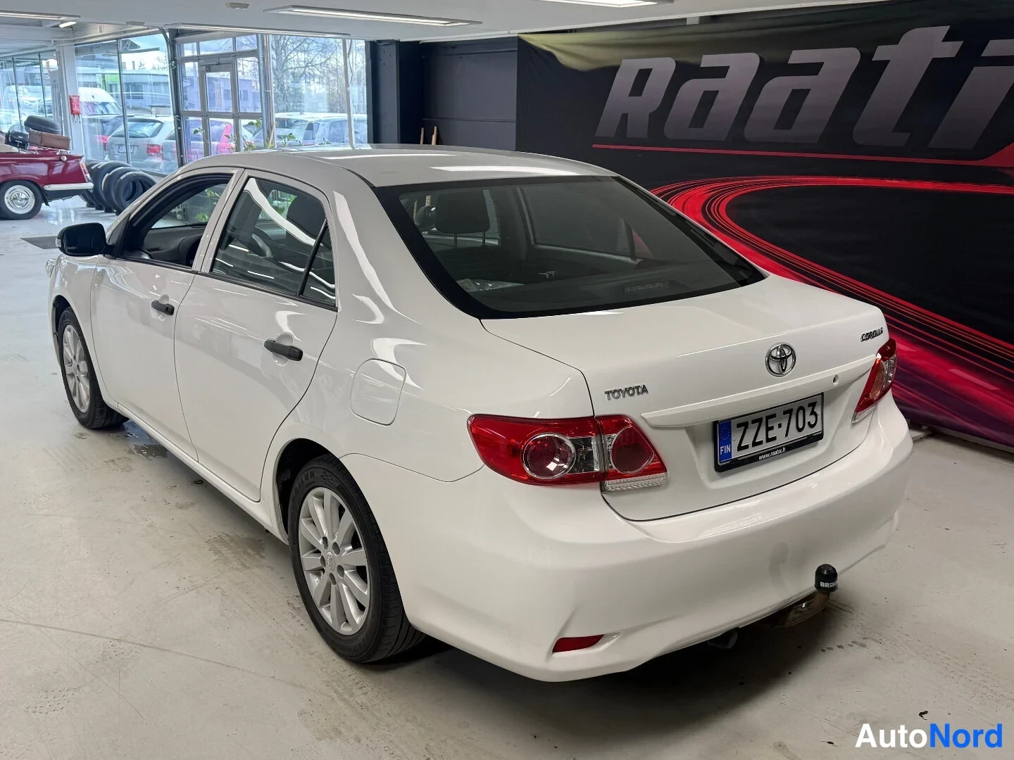 Takaviisto: Valkoinen Toyota Corolla -sedan takaa kolmasosakulmasta, takavalot ja rekisteritunnus näkyvissä.