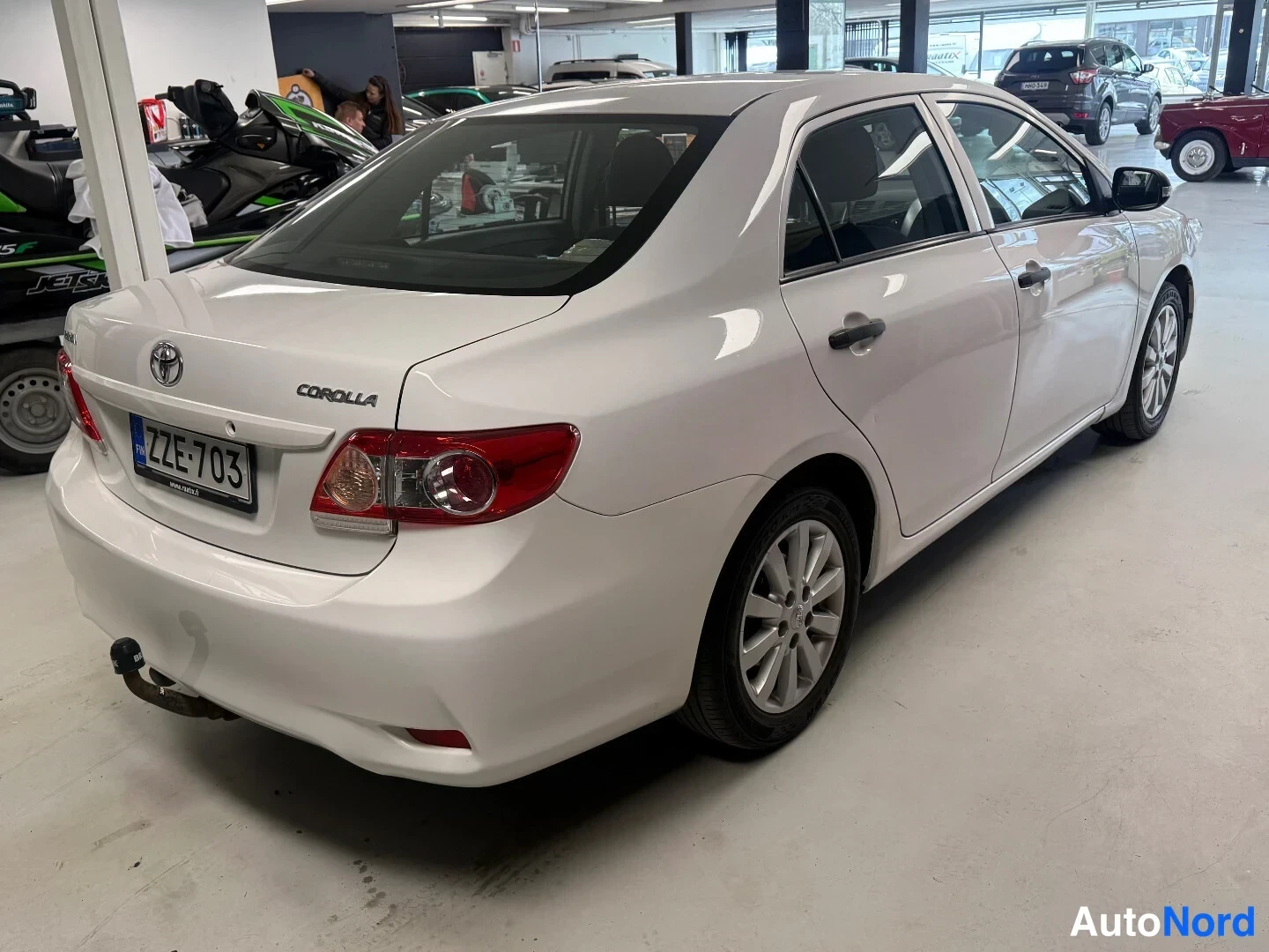 Takaviisto: Valkoinen Toyota Corolla -sedan takaa vasemmalta, takapontti ja rekisteritunnus näkyvissä.