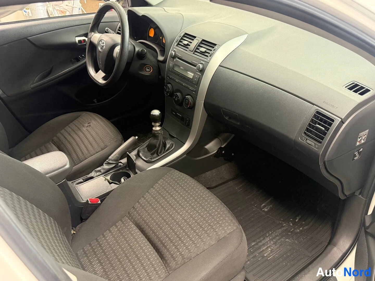Muu: Auton sisätilat: tummat kangasistuimet, manuaalivaihtopyörähdys ja Toyota-ohjauspyörä.