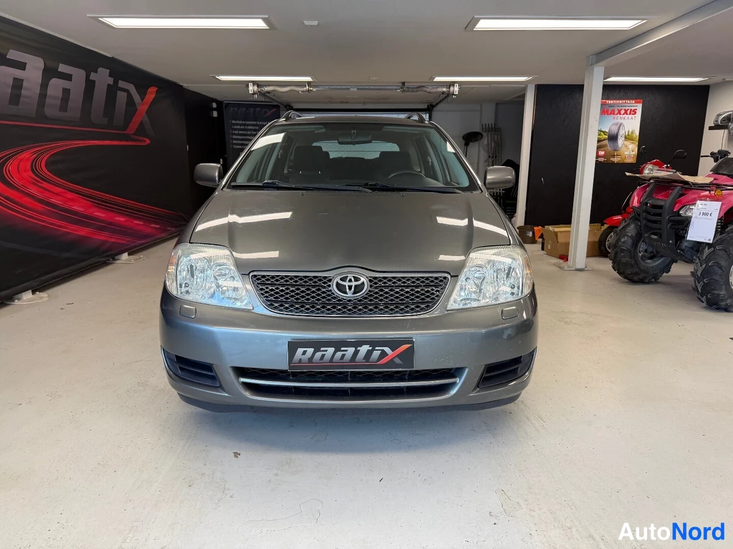 Edestä: Toyota Corolla -farmarin etupää kuvattuna suoraan edestä sisätiloissa; harmaa kori, Toyota-merkki säleikössä ja ajovalot näkyvät.
