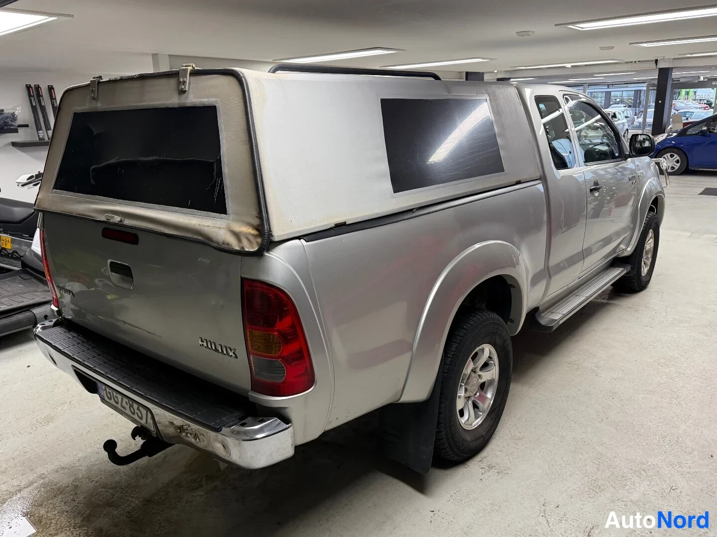 Takaviisto: Toyota Hilux -nakun takaosa ja vasen sivu takaa kolmasosakulmasta sisähallissa, takapuskurissa veto koukku.
