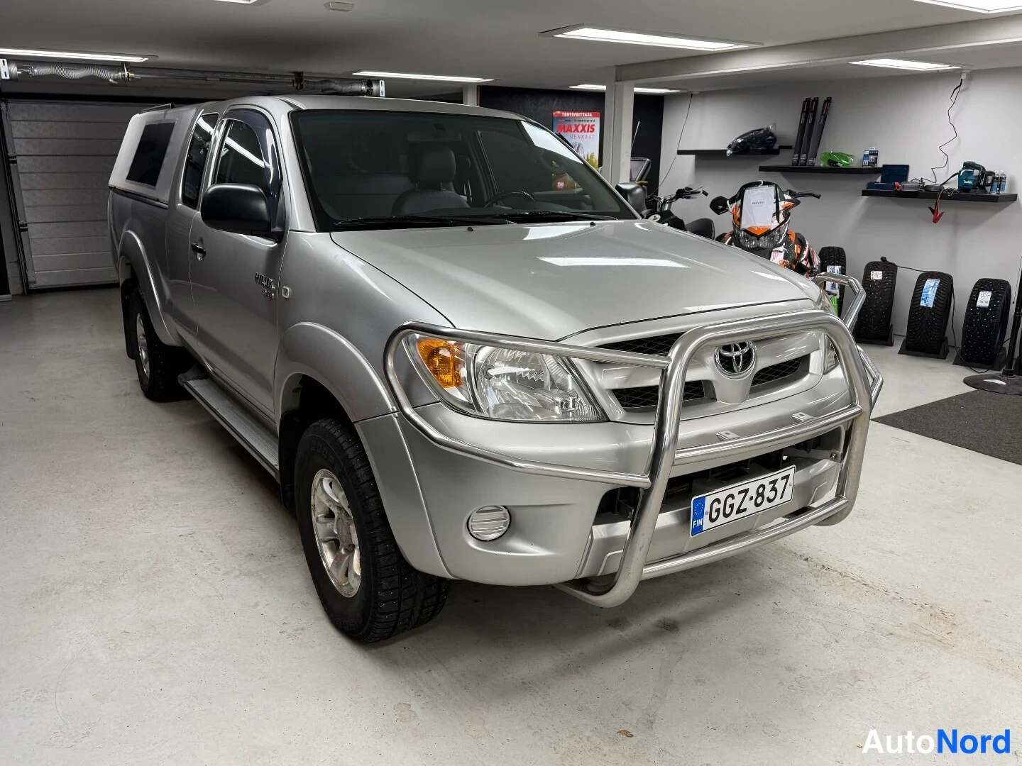 Etuviisto, nokka oikealle: Toyota Hilux -nakku edestä oikealta kolmasosakulmasta, hopeisenä, kromietukaarella, rekisteri.